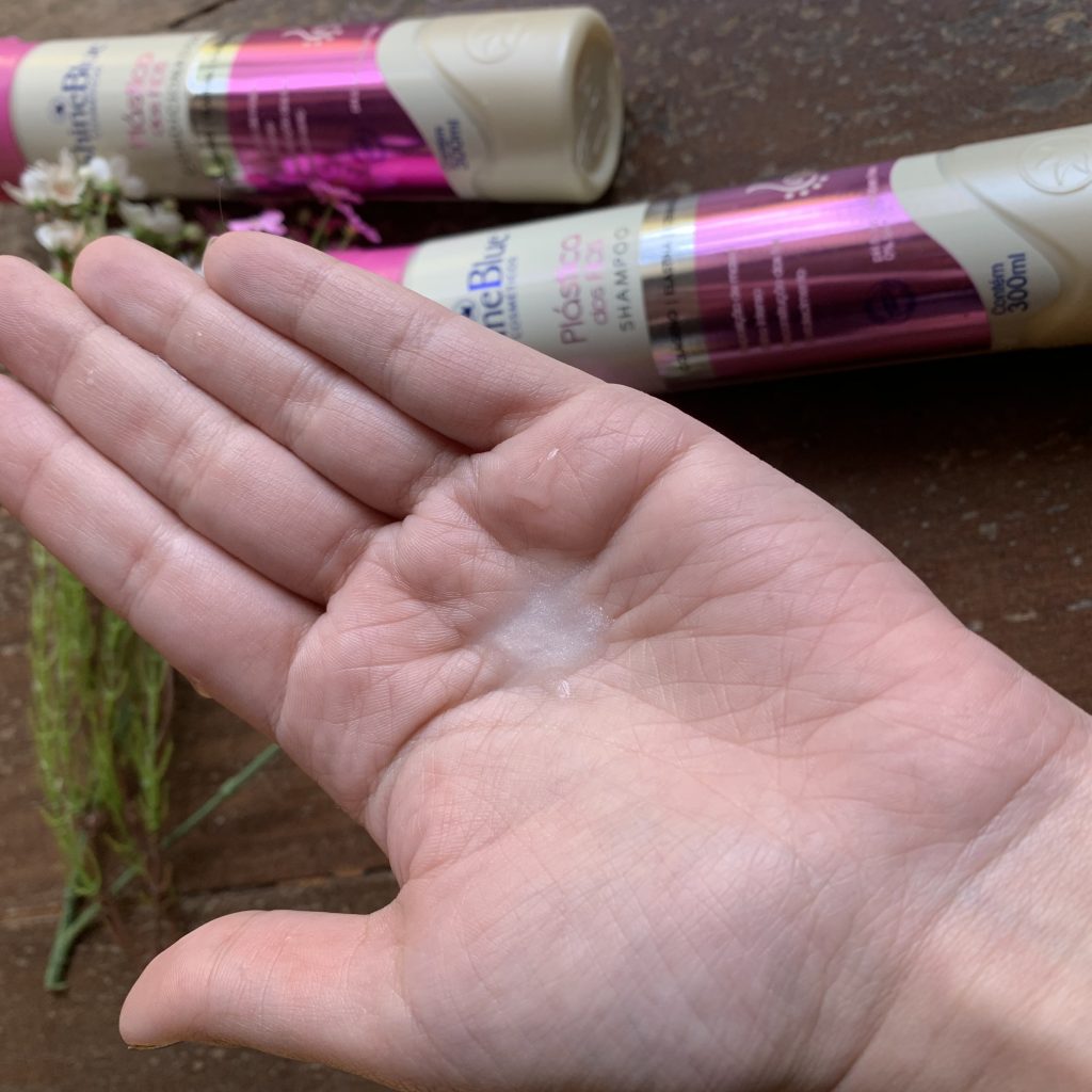 A foto mostra uma pequena aplicação do shampoo Plástica dos Fios na Shine Blue na palma da mão, ela é esbranquiçada e fluida. 